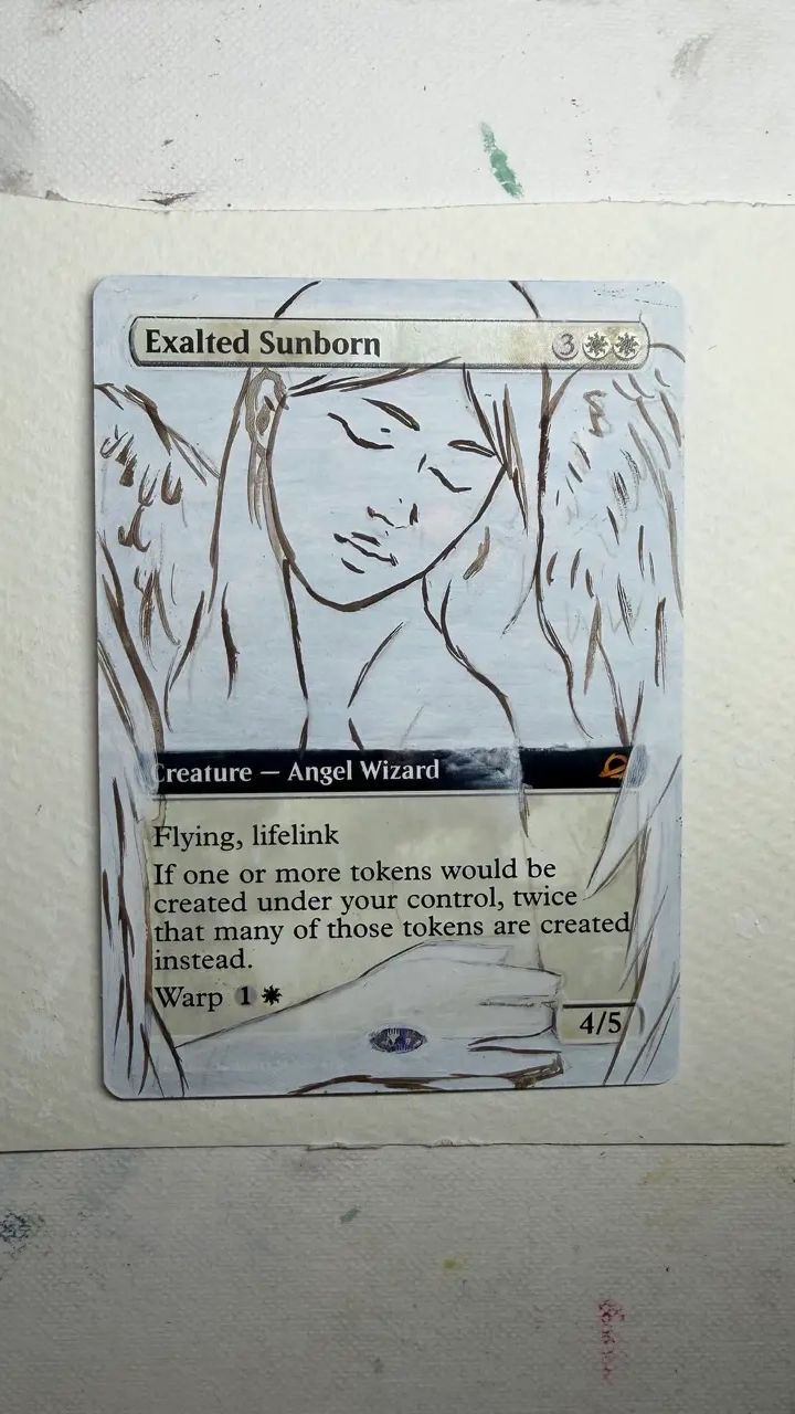 A trading card is placed on a light-textured surface. The artwork shows a line-drawn figure with large, sweeping wings extending outward. The lower portion includes a hand holding what appears to be a staff or elongated object. The piece is in an early painted stage, with light washes of color and visible sketch lines.